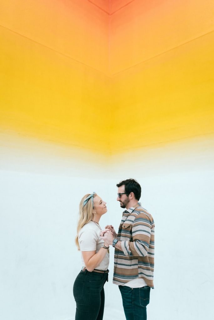 man and woman kissing beside yellow wall