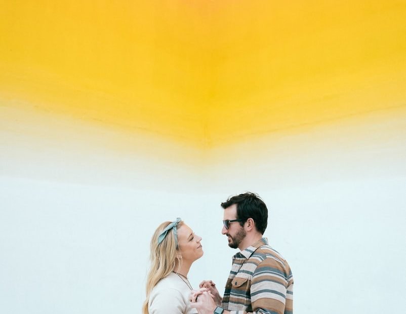 man and woman kissing beside yellow wall